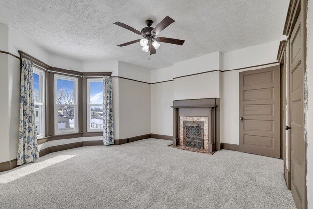 unfurnished living room featuring baseboards, light colored carpet, a fireplace with flush hearth, ceiling fan, and a textured ceiling