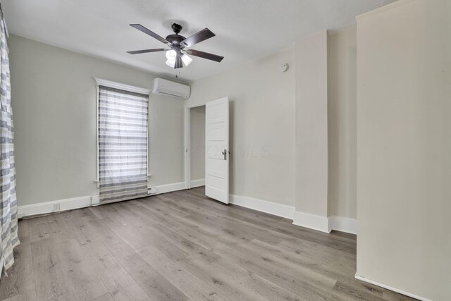 unfurnished room featuring light wood-style floors, ceiling fan, baseboards, and an AC wall unit