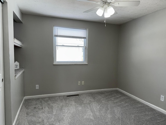 carpeted empty room featuring a textured ceiling, a ceiling fan, visible vents, and baseboards