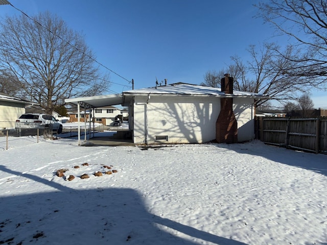 snow covered house with a carport, fence, and a chimney