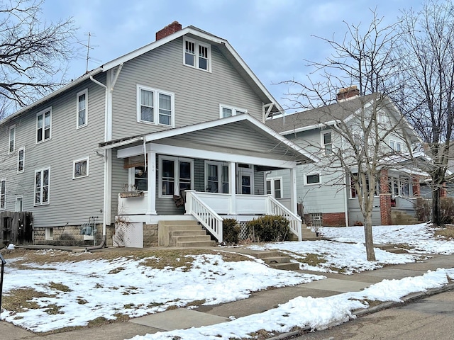 american foursquare style home featuring a chimney and covered porch