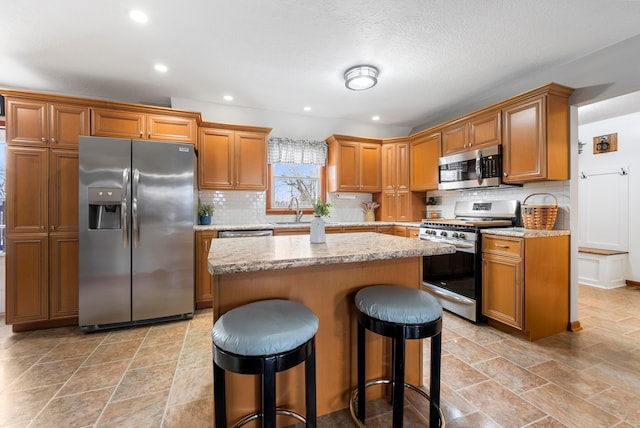 kitchen featuring a sink, a kitchen bar, a center island, brown cabinets, and stainless steel appliances