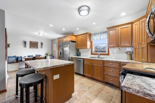 kitchen with decorative backsplash, appliances with stainless steel finishes, a sink, a breakfast bar area, and a center island