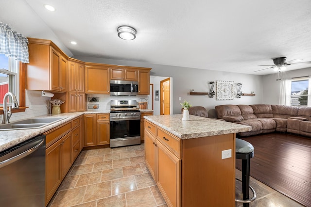 kitchen featuring light countertops, a sink, a ceiling fan, a center island, and stainless steel appliances