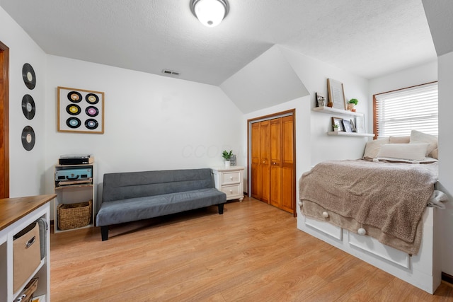 bedroom with a closet, a textured ceiling, visible vents, light wood-type flooring, and vaulted ceiling