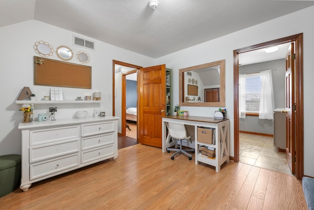 office area with a textured ceiling, visible vents, baseboards, light wood-style floors, and vaulted ceiling