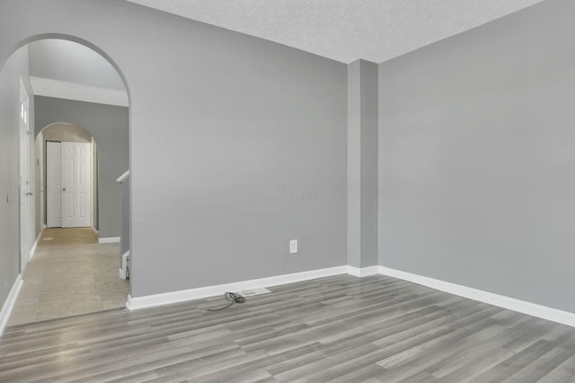 spare room featuring arched walkways, a textured ceiling, baseboards, and light wood-style floors