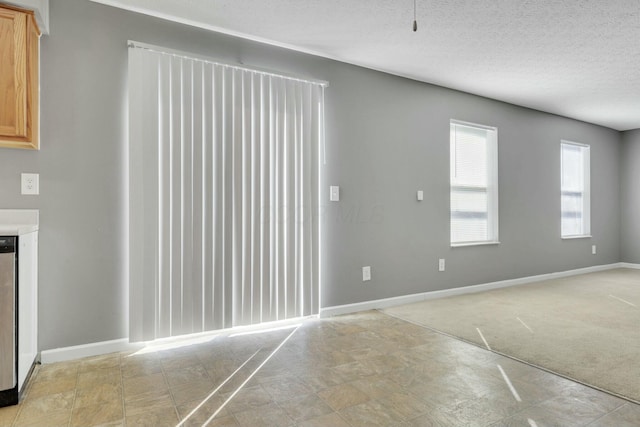 spare room with a textured ceiling, light carpet, and baseboards