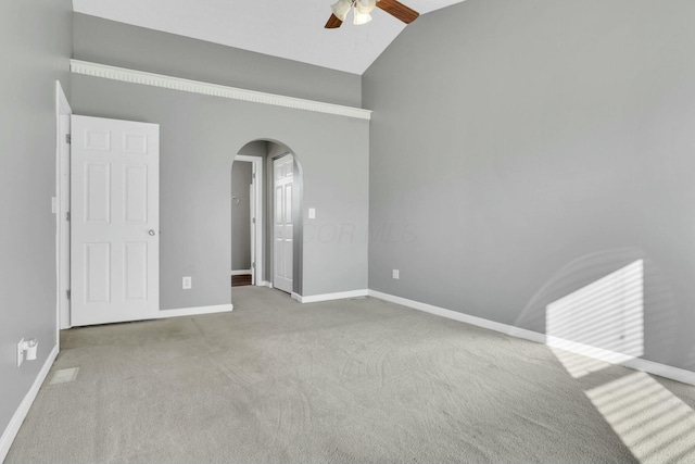 unfurnished bedroom featuring light carpet, baseboards, arched walkways, a ceiling fan, and high vaulted ceiling