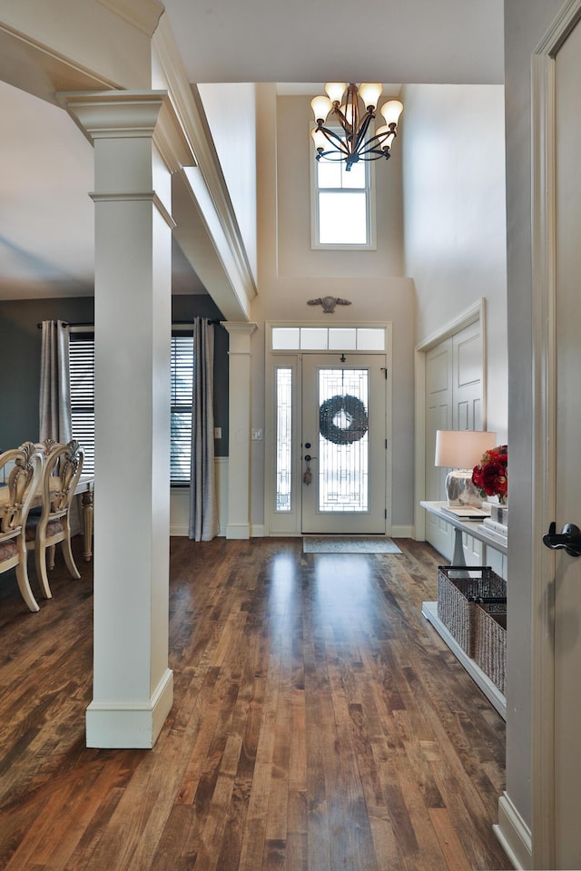 foyer with decorative columns, baseboards, wood finished floors, an inviting chandelier, and a high ceiling