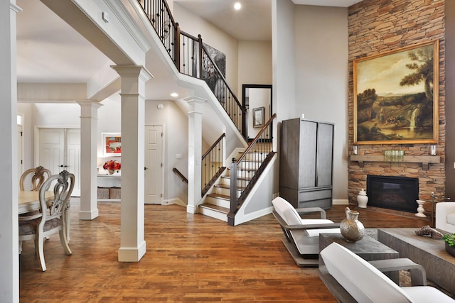 interior space with a high ceiling, a fireplace, wood finished floors, stairs, and ornate columns