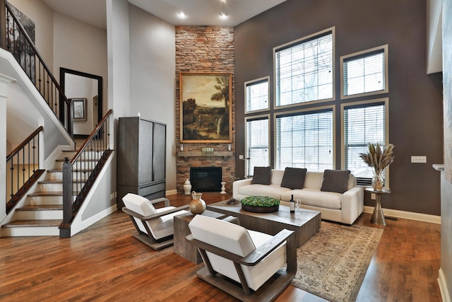 living area featuring stairway, dark wood-style flooring, a towering ceiling, and a stone fireplace