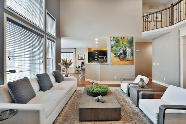 living room with baseboards, visible vents, a high ceiling, and wood finished floors