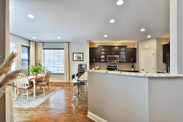 kitchen with dark brown cabinetry, stove, decorative backsplash, dark wood-style floors, and stainless steel microwave