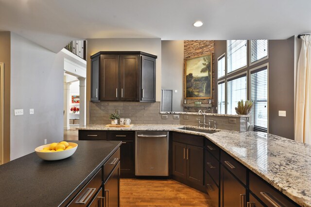 kitchen featuring dark brown cabinetry, wood finished floors, a sink, dishwasher, and tasteful backsplash