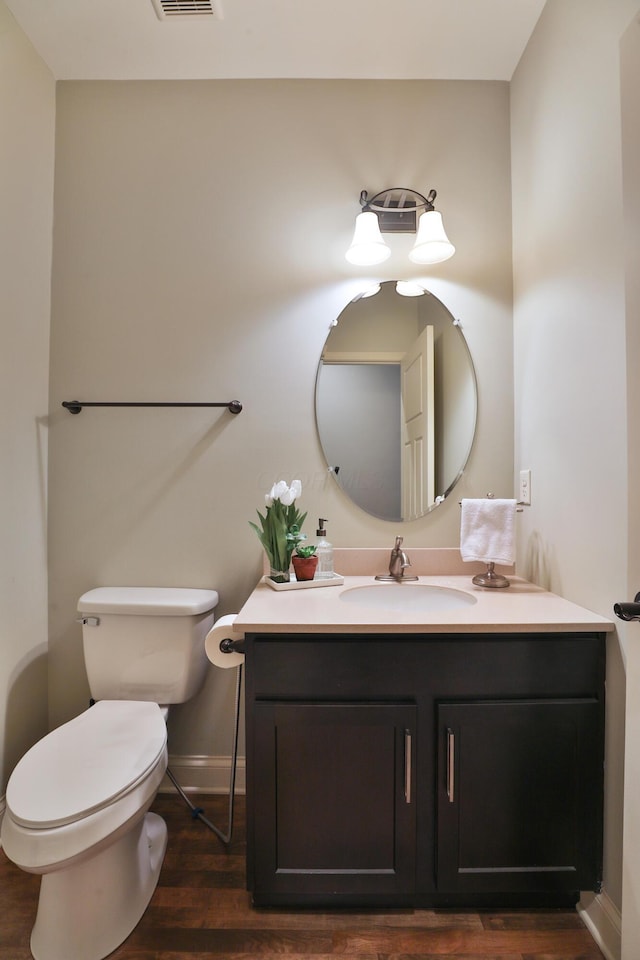 bathroom featuring visible vents, baseboards, toilet, wood finished floors, and vanity