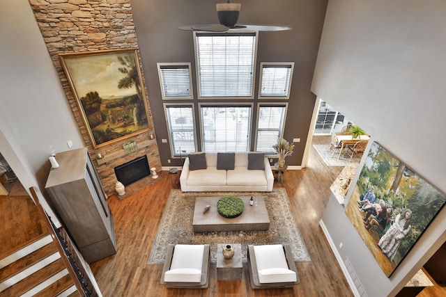 living room featuring a glass covered fireplace, a towering ceiling, baseboards, and wood finished floors