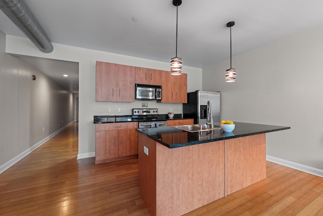 kitchen featuring a sink, light wood-style floors, appliances with stainless steel finishes, a center island with sink, and pendant lighting