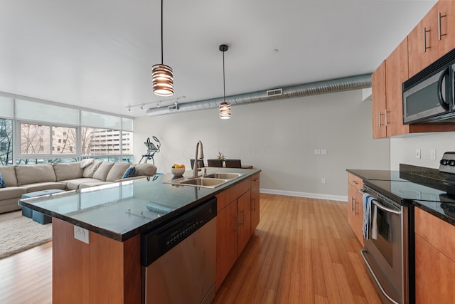 kitchen featuring open floor plan, stainless steel appliances, hanging light fixtures, and a sink