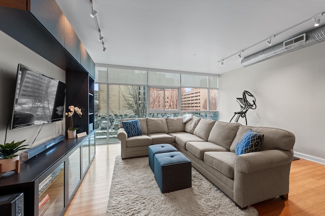 living room featuring expansive windows, baseboards, track lighting, and wood finished floors