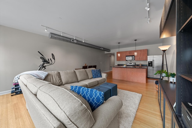 living area featuring track lighting, baseboards, and light wood finished floors