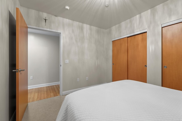 bedroom featuring baseboards, two closets, and wood finished floors