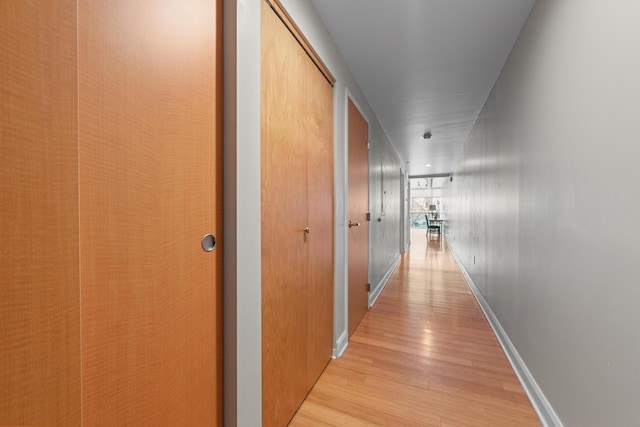 corridor featuring light wood-type flooring and baseboards