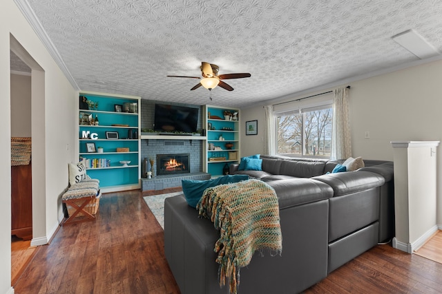 living area featuring a textured ceiling, ceiling fan, a fireplace, ornamental molding, and dark wood finished floors