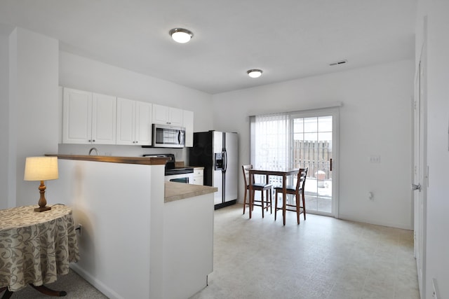 kitchen featuring stainless steel microwave, a peninsula, fridge with ice dispenser, white cabinetry, and range with electric stovetop