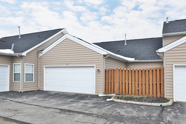 exterior space featuring a shingled roof, fence, and community garages