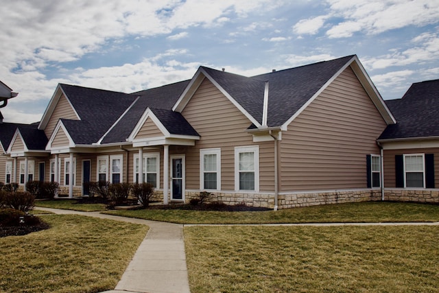 townhome / multi-family property featuring stone siding, a shingled roof, and a front yard