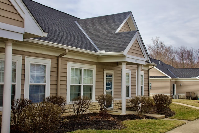 view of side of home featuring stone siding, roof with shingles, and cooling unit