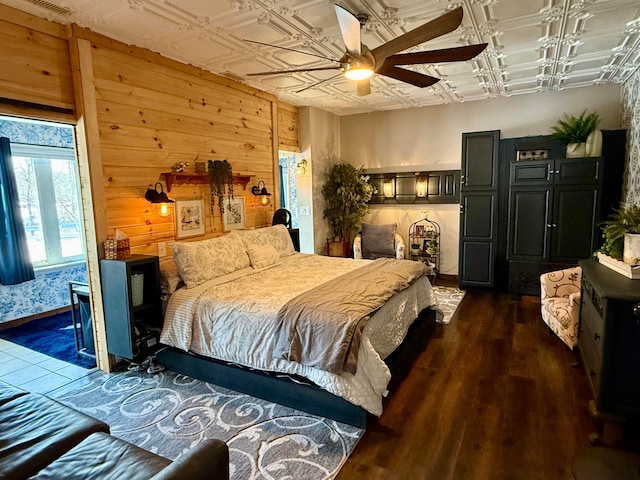 bedroom featuring an ornate ceiling, dark wood finished floors, wooden walls, and a ceiling fan