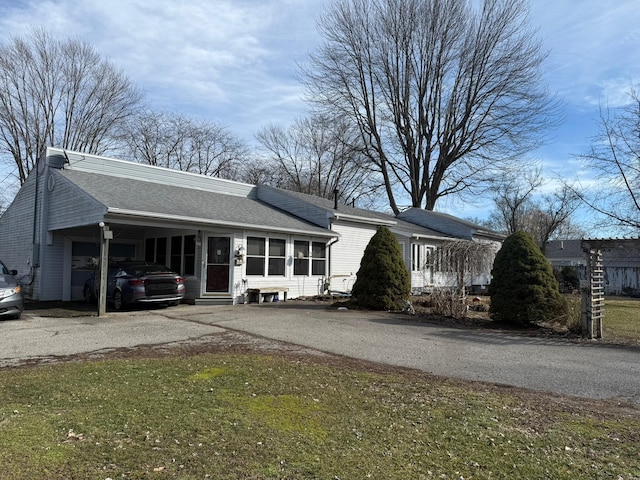 view of front of property with a sunroom, roof with shingles, driveway, and a front lawn