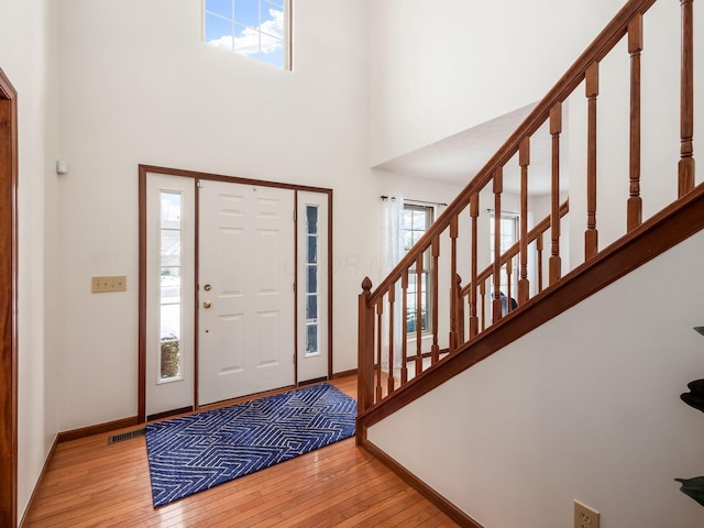 entrance foyer with a towering ceiling, light wood-style floors, visible vents, and baseboards