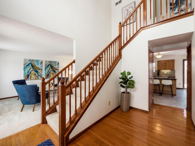 staircase featuring a towering ceiling, visible vents, baseboards, and wood finished floors