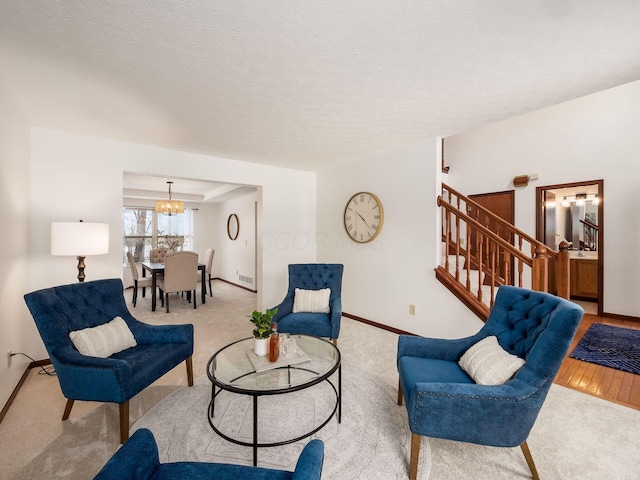 living room featuring a textured ceiling, a notable chandelier, light colored carpet, baseboards, and stairway