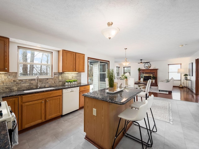 kitchen featuring white appliances, a kitchen island, brown cabinets, decorative light fixtures, and a sink