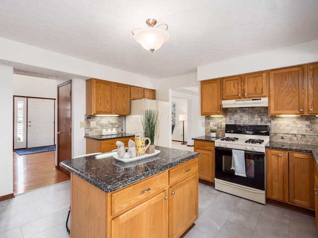 kitchen featuring a center island, range with gas cooktop, brown cabinets, freestanding refrigerator, and under cabinet range hood