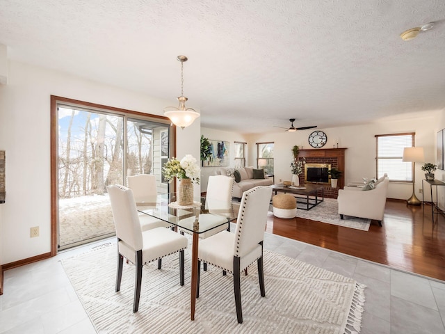 dining space with a fireplace, light tile patterned floors, ceiling fan, a textured ceiling, and baseboards