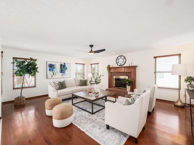 living room with dark wood-style floors, a brick fireplace, baseboards, and a ceiling fan