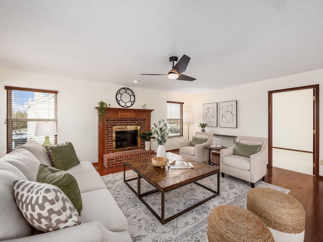 living room with a textured ceiling, ceiling fan, a brick fireplace, and light wood-style floors