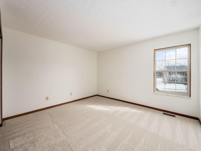 spare room featuring carpet floors, visible vents, a textured ceiling, and baseboards