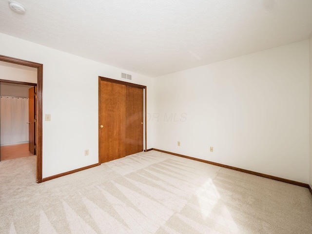 unfurnished bedroom featuring light colored carpet, a closet, visible vents, and baseboards