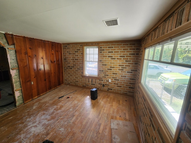 empty room featuring brick wall, hardwood / wood-style flooring, and a wealth of natural light