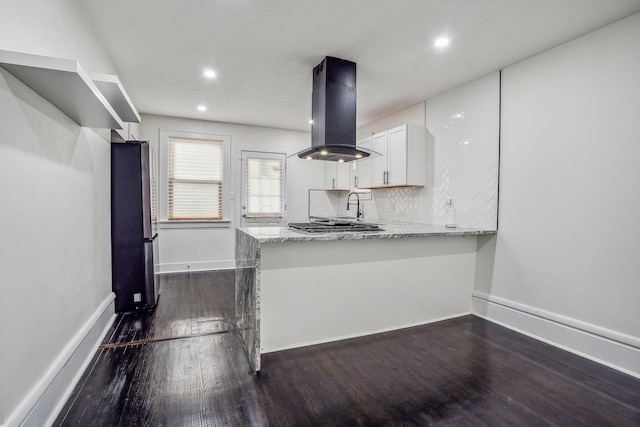 kitchen featuring white cabinetry, kitchen peninsula, stainless steel refrigerator, light stone countertops, and island range hood