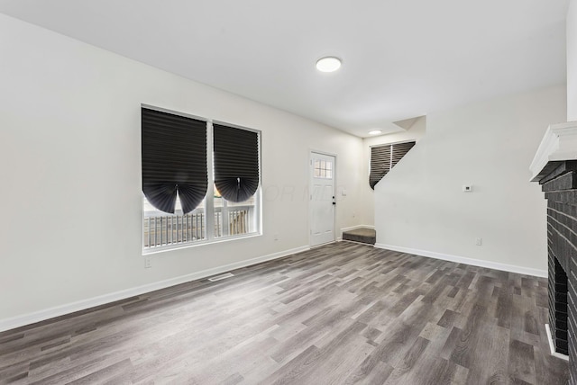 unfurnished living room featuring stairs, a fireplace, baseboards, and wood finished floors