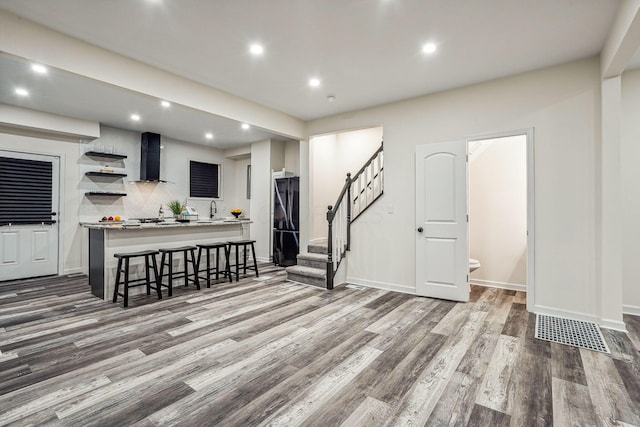 kitchen with wall chimney range hood, sink, black fridge, and hardwood / wood-style floors