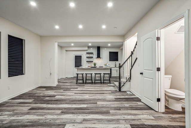 interior space featuring dark wood-type flooring, a breakfast bar, and wall chimney range hood