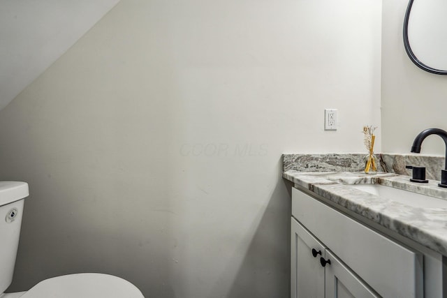 bathroom with toilet, vanity, and vaulted ceiling